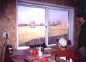 Adult male in a wheelchair by his farm shopâ€™s desk looking out a large window to the left of which is a wall-mounted electrical outlet plus switch at sitting-reachable height.