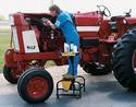 An adult male stands on the productâ€™s top step to work on a tractor engine.