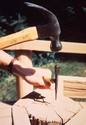 A hammer is ready to strike a nail-set being held upright by the magnet which protrudes out from the length of rubber tubing that a hand is grasping.