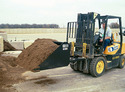 Black scoop bucket with load of dirt mounted on yellow & black forklift being driven by man in dark blue pants & light blue polo shirt.