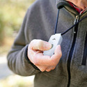 Person in a gray jacket holding a Personal Safety Alert System for Workers in their right hand with their thumb on the alert-button