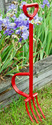 All red metal EarthLifter Spading Fork standing up against a raised bed of purple irises